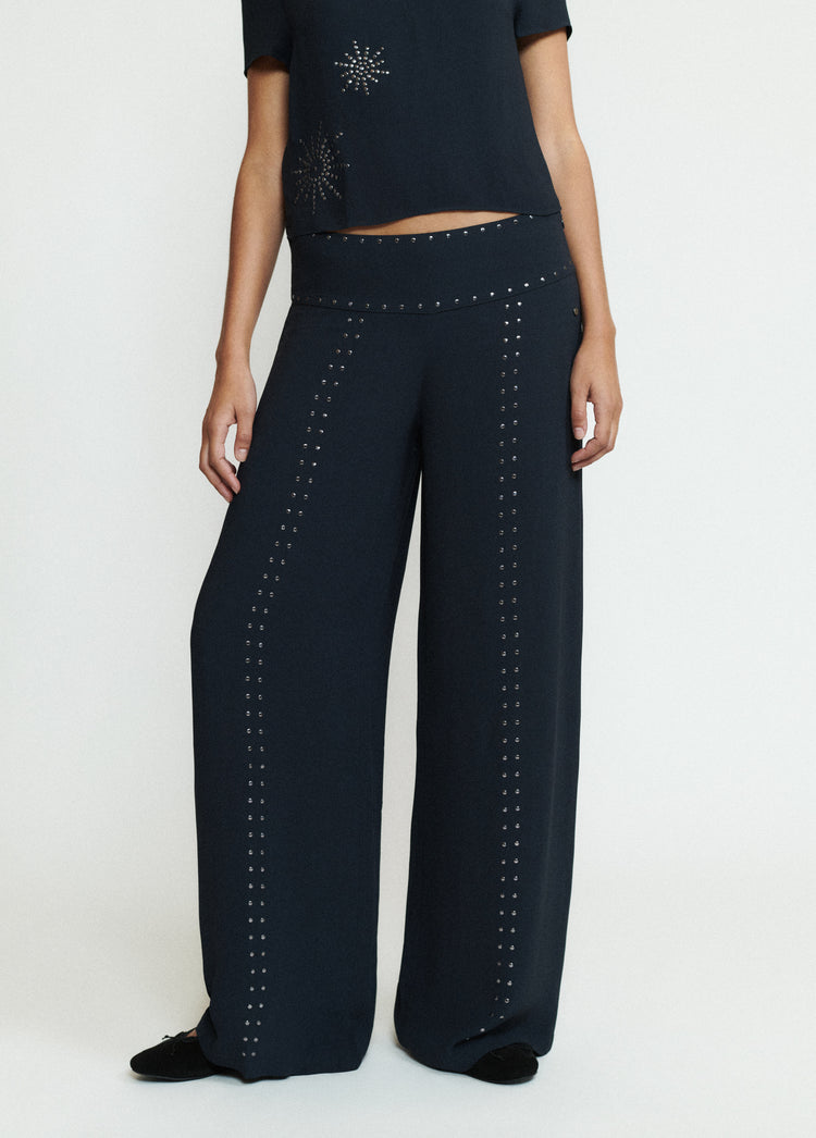 Pantalón largo negro de pierna ancha con filas de tachas en el bajo sobre modelo