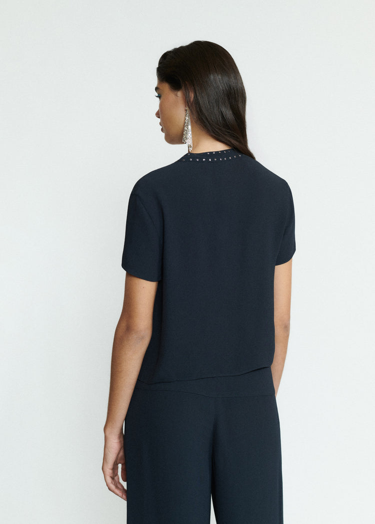 Blusa de manga corta en negro vista por detrás mostrando el detalle de tachas en el cuello