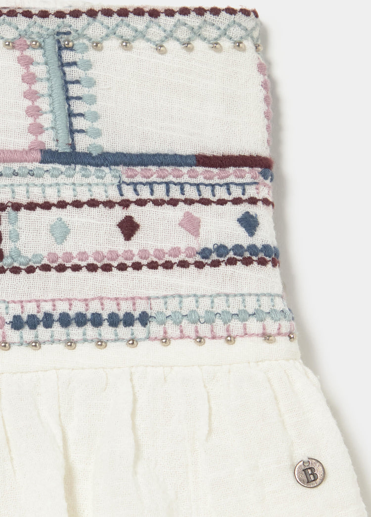 Detalle de la cintura de la falda blanca con bordados geométricos multicolores y abalorios metálicos