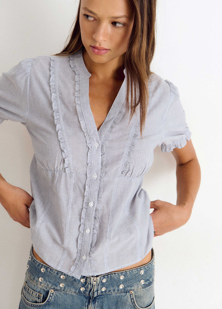 Blusa de manga corta en azul con detalles de volantes y botones sobre modelo