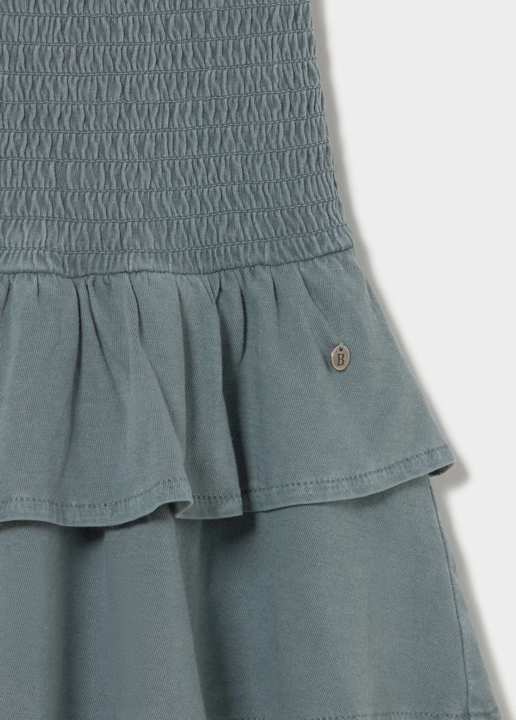 Vestido smock de color verdoso con detalle de volantes y botón decorativo en la parte superior