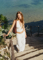 Pantalón pareo de color blanco con detalle de concha lucido en una escalera junto al mar