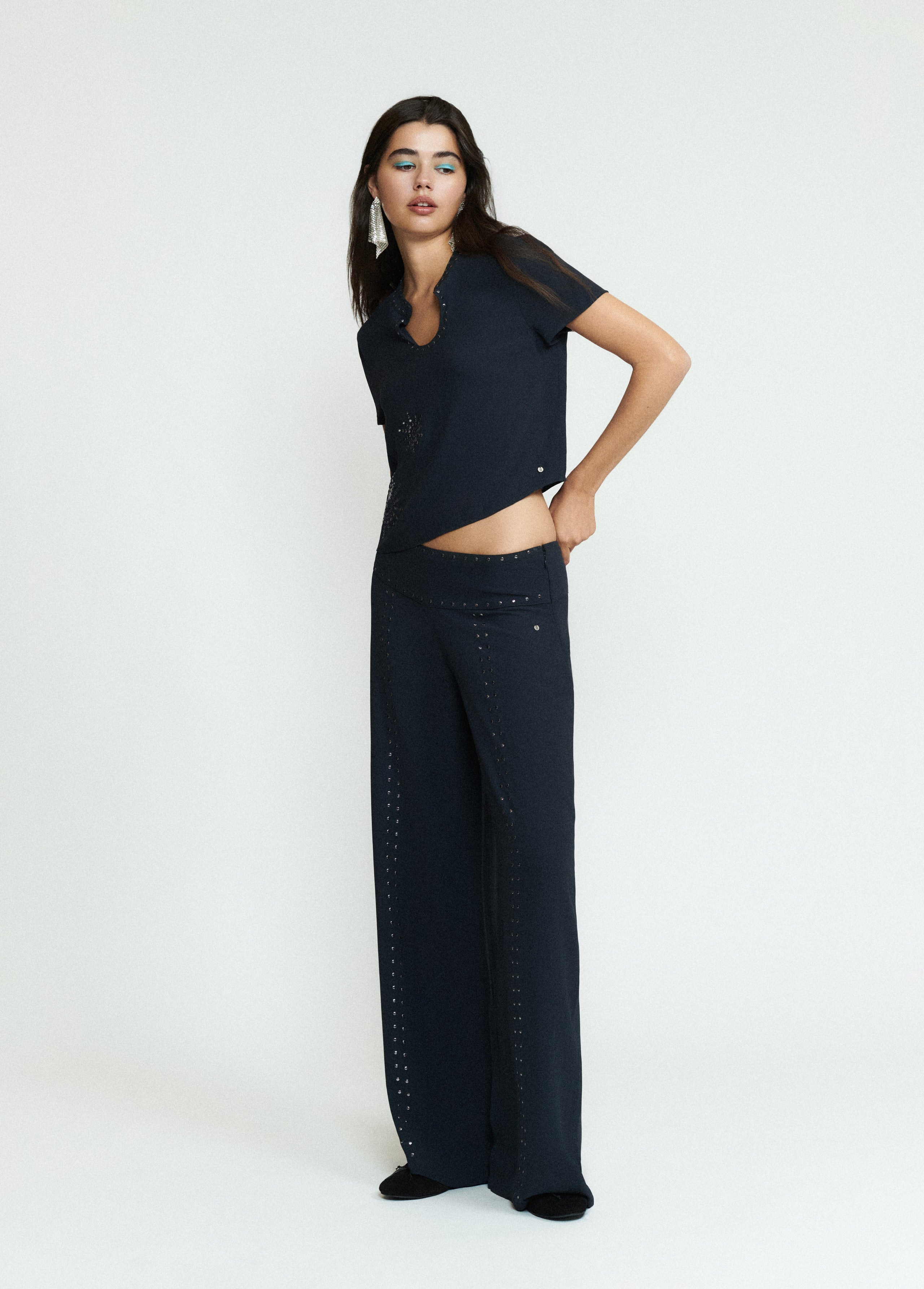 Pantalón largo negro de corte amplio con detalles de tachas sobre modelo
