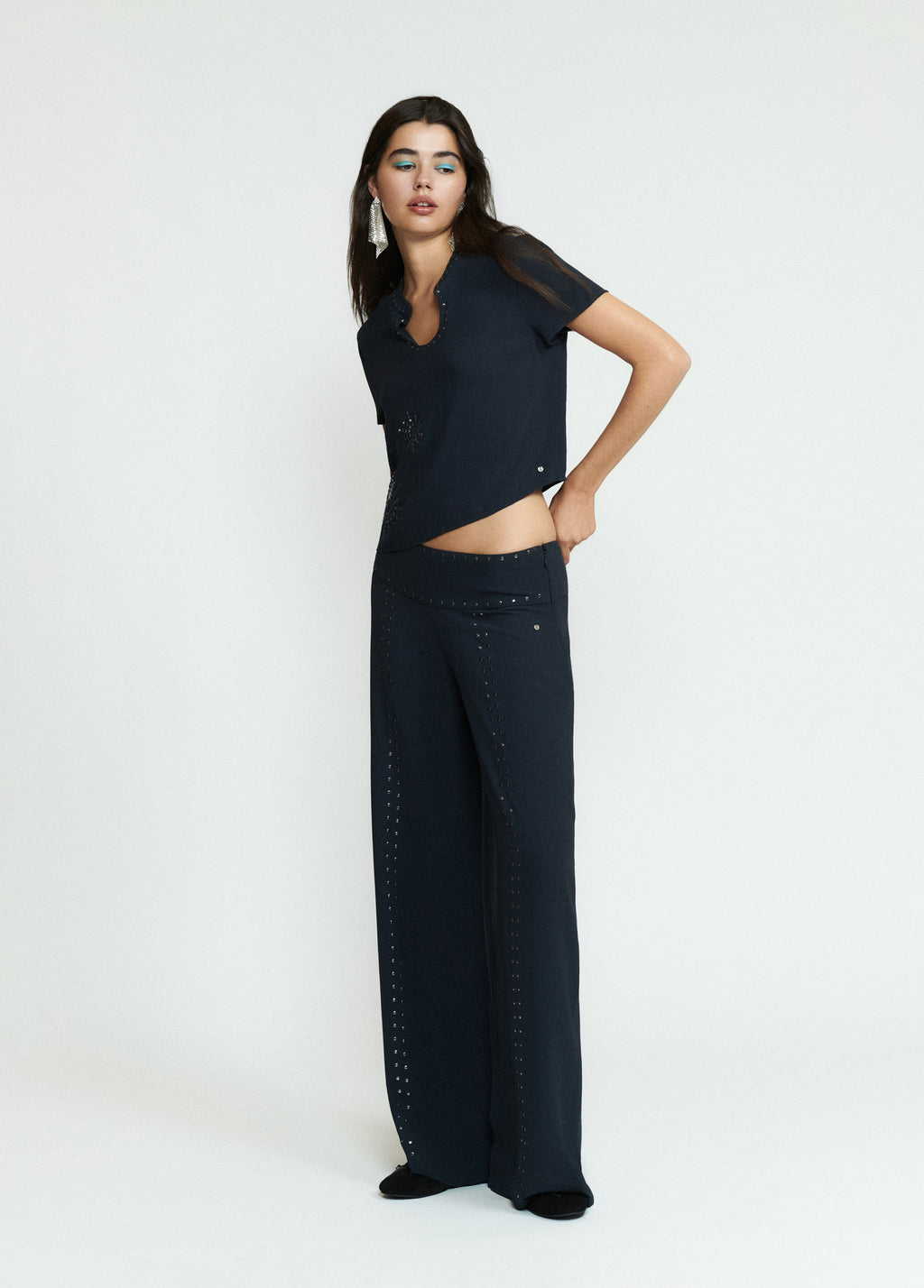 Pantalón largo negro de corte amplio con detalles de tachas sobre modelo
