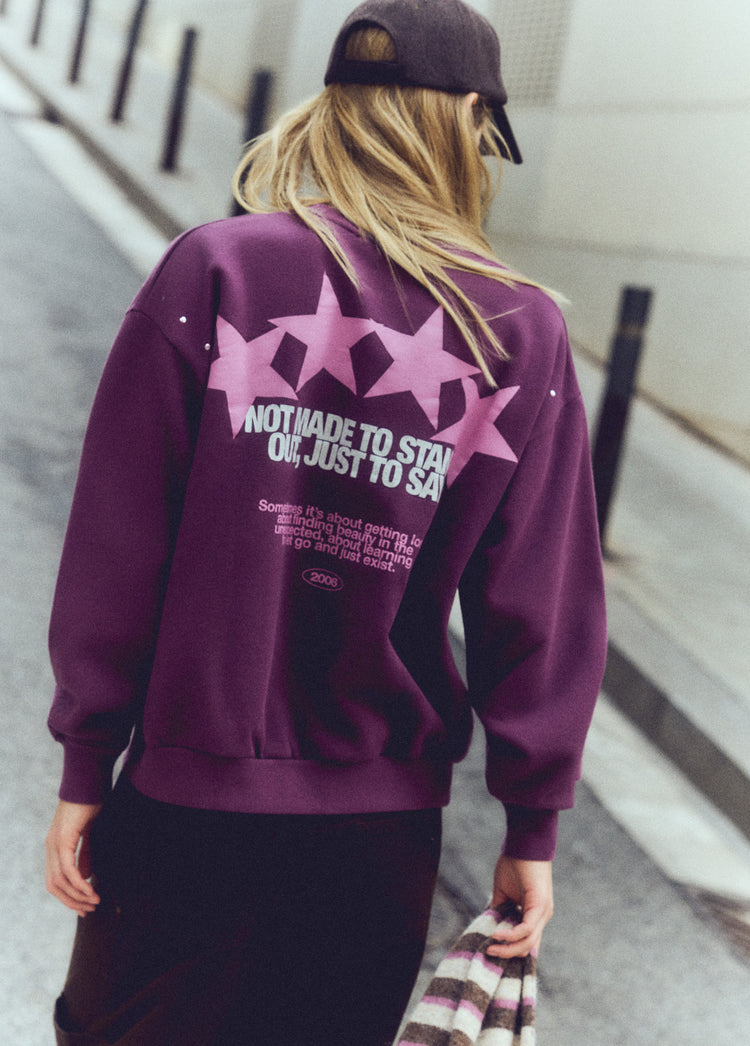 Sudadera de color granate con estampado de estrellas y texto en la espalda vista sobre modelo