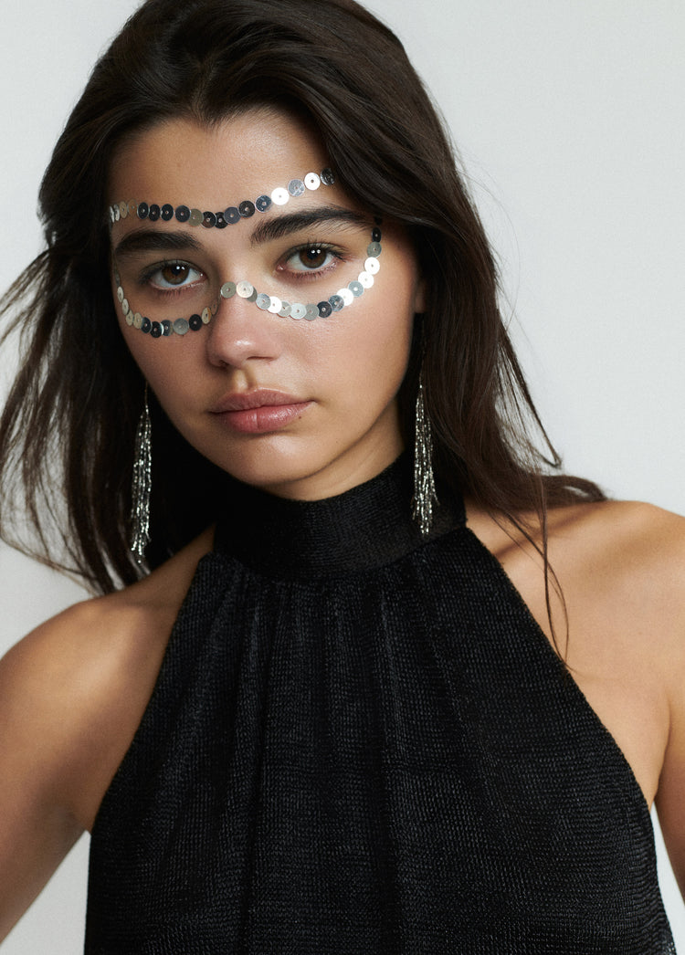Top halter de brillo en negro sobre modelo con adornos de lentejuelas en el rostro