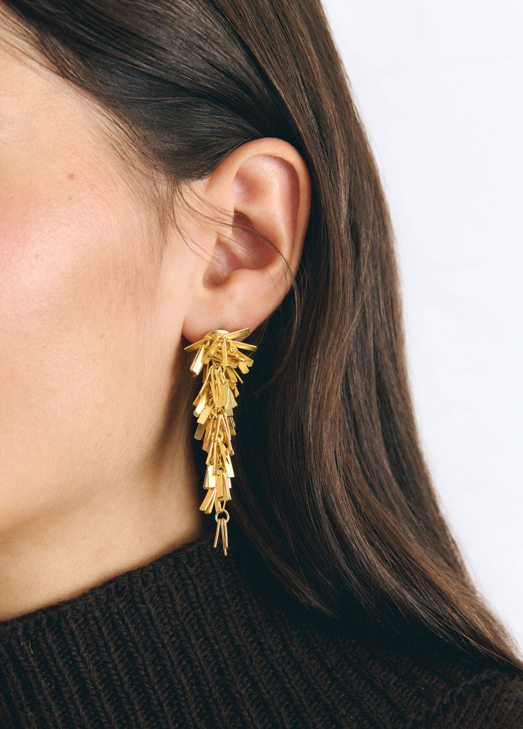Pendientes dorados de colgante con diseño de pompón vistos en primer plano sobre la oreja