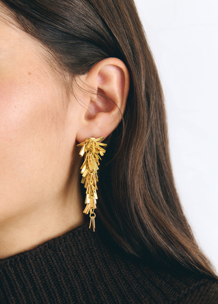 Pendientes dorados de colgante con diseño de pompón vistos en primer plano sobre la oreja