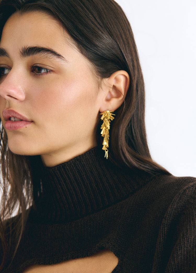 Pendientes dorados de colgante con diseño de pompón lucidos sobre modelo
