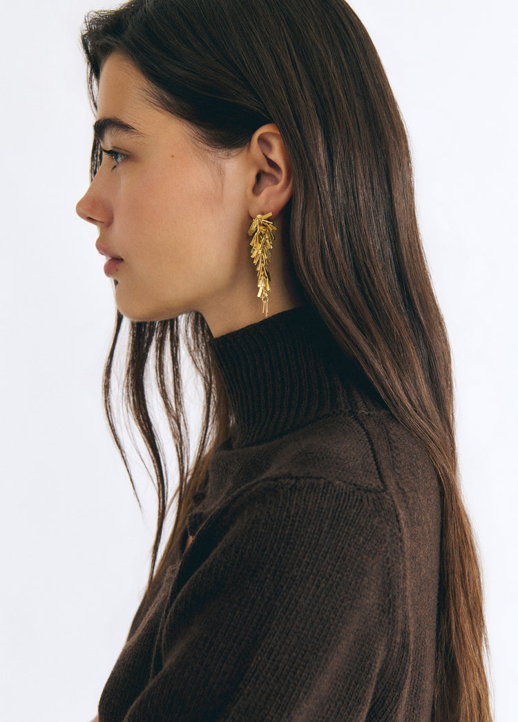 Pendientes dorados de colgante con diseño de pompón vistos en perfil sobre modelo