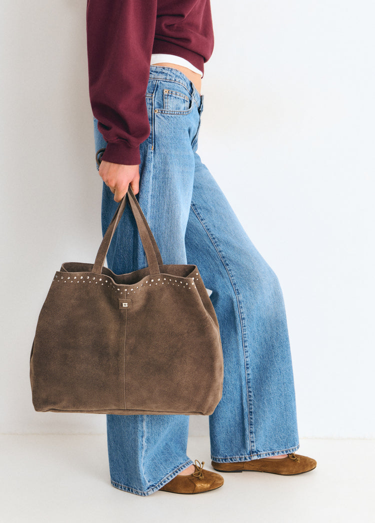 Bolso shopper de color topo con tachas sostenido de las asas sobre modelo