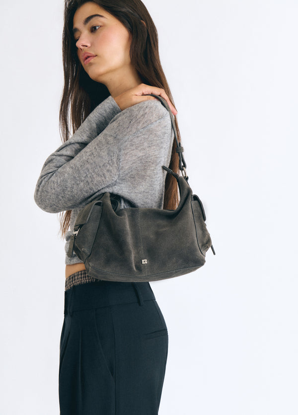 Bolso de hombro en gris oscuro con bolsillos laterales, luciendo su perfil sobre modelo
