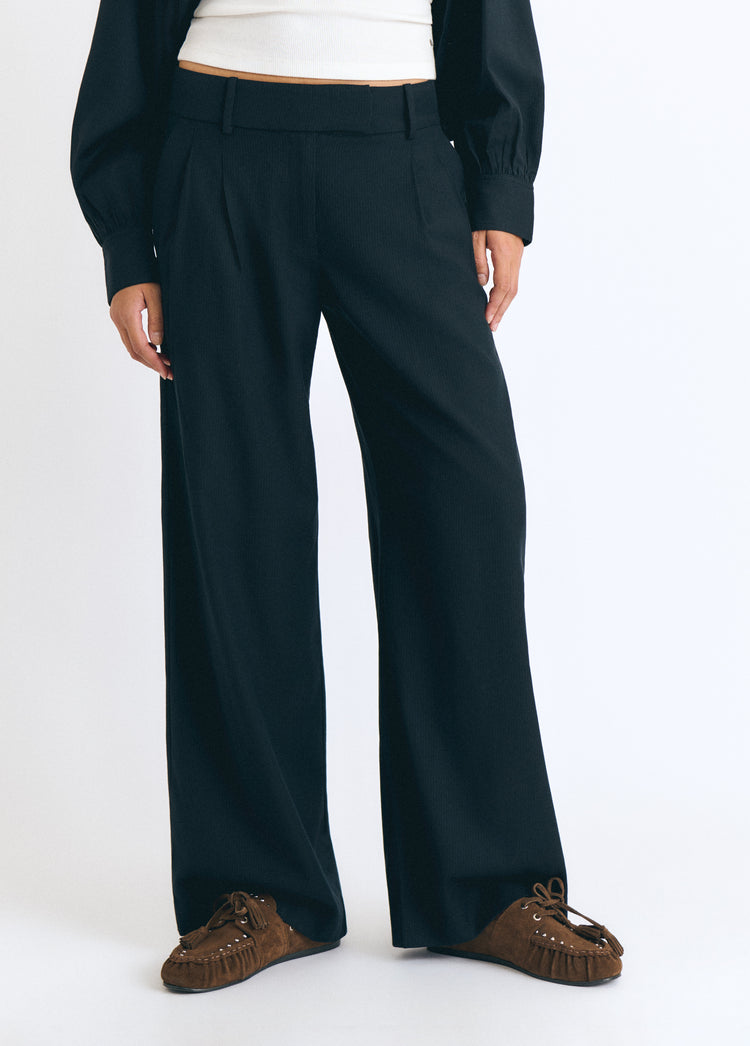 Pantalón de pinzas en azul marino sobre modelo con top blanco y mocasines