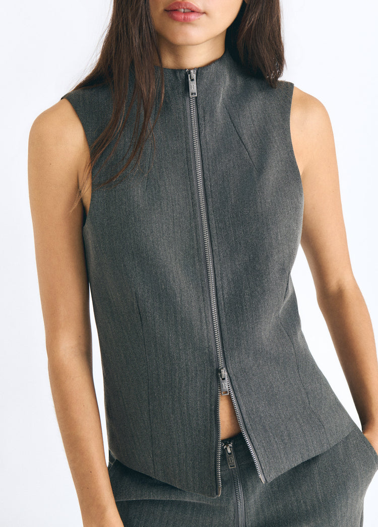 Top gris sin mangas con cremallera frontal y cuello alto visto en primer plano sobre modelo