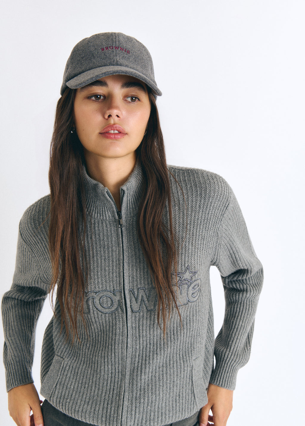 Gorra de fieltro gris con bordado frontal lucida sobre modelo junto a su jersey de cremallera
