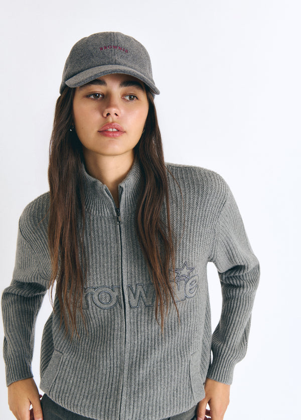 Gorra de fieltro gris con bordado frontal lucida sobre modelo junto a su jersey de cremallera