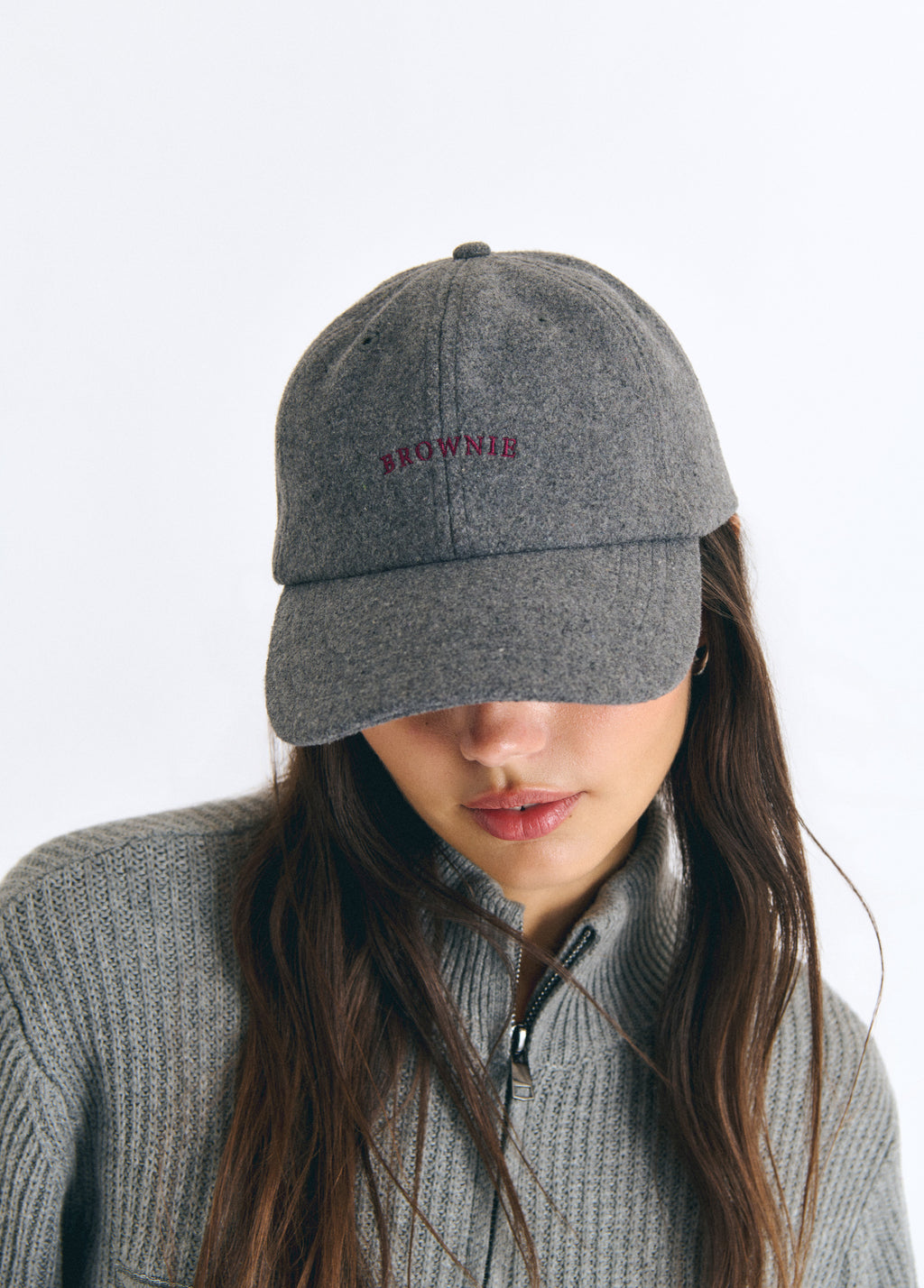 Gorra de fieltro gris con bordado rojo en el frente lucida sobre modelo con jersey de cremallera