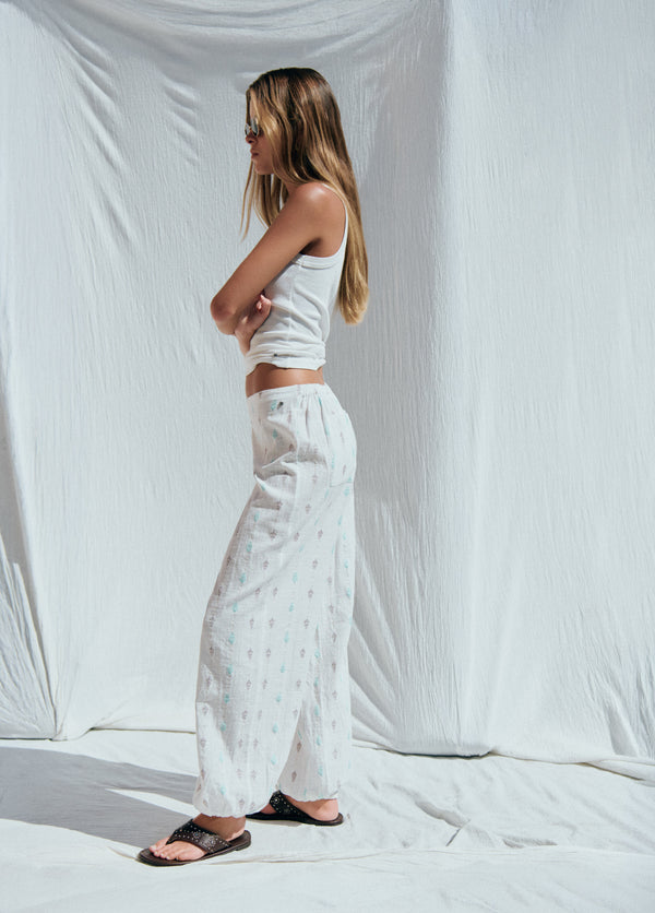 Pantalón bombacho blanco con bordados, visto de perfil sobre fondo liso